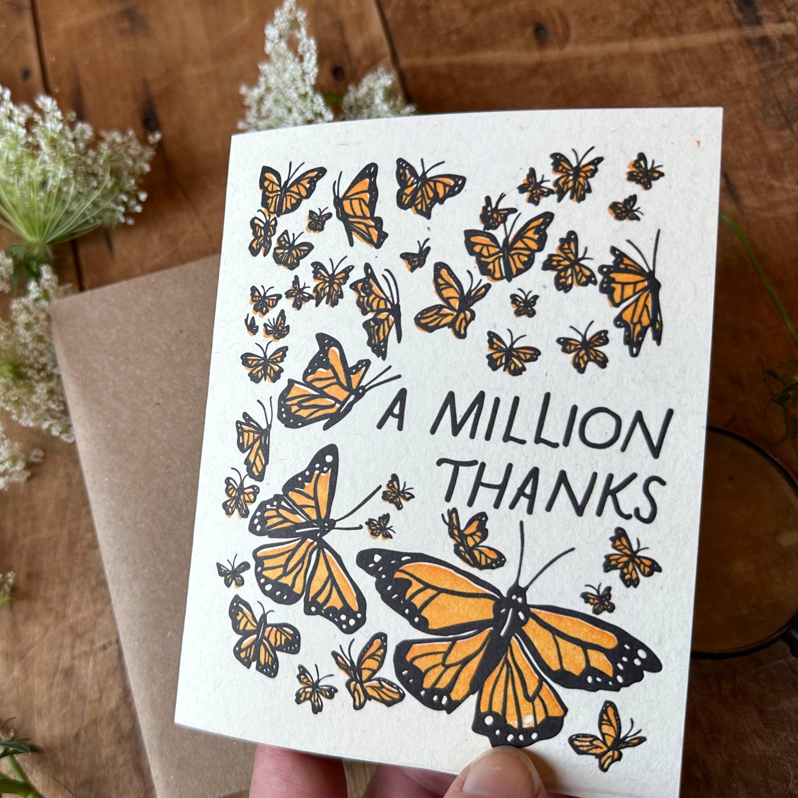 Card with butterfly design and 'A Million Thanks' text on a wooden surface with flowers and a magnifying glass.