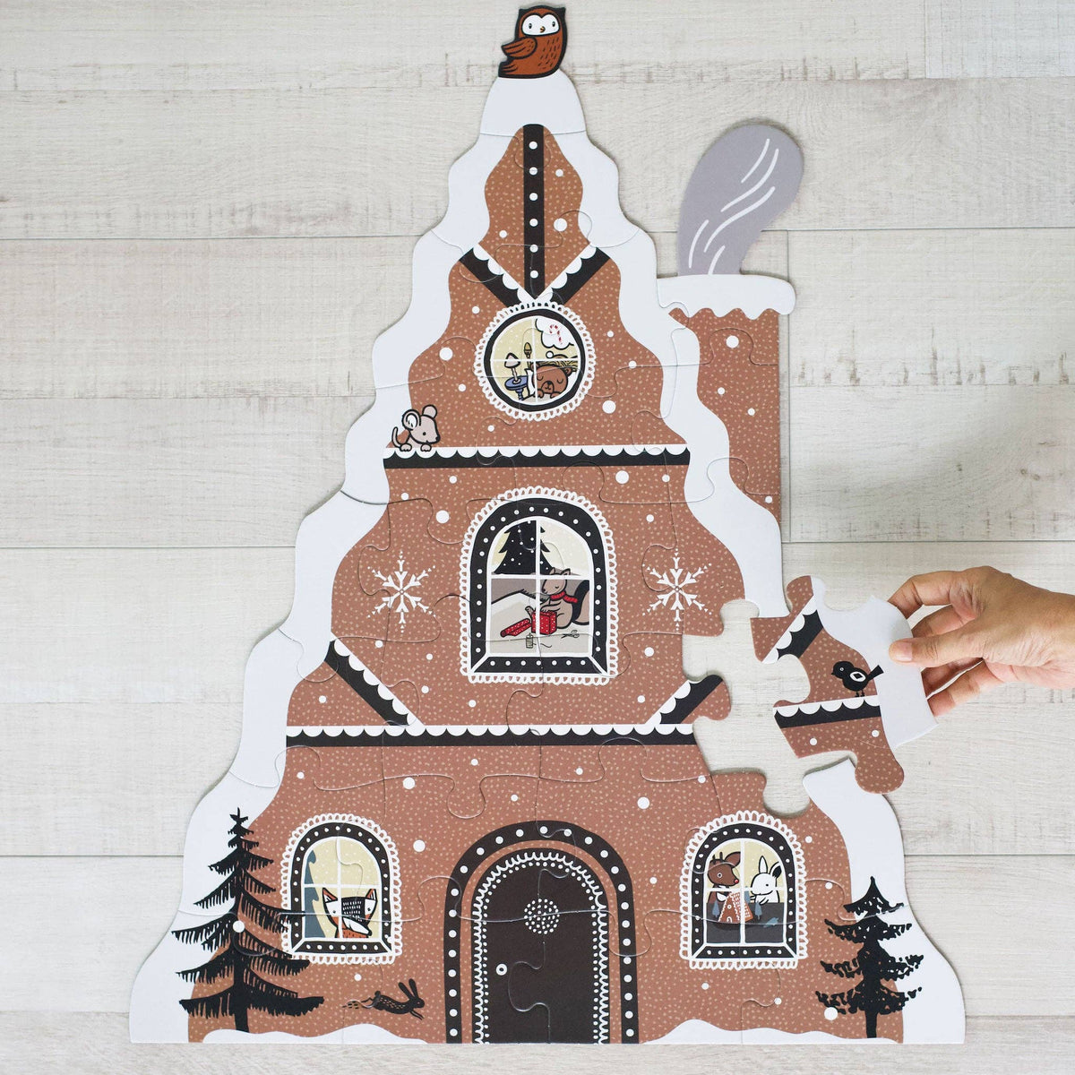 Gingerbread house puzzle with a hand placing a piece on a wooden surface
