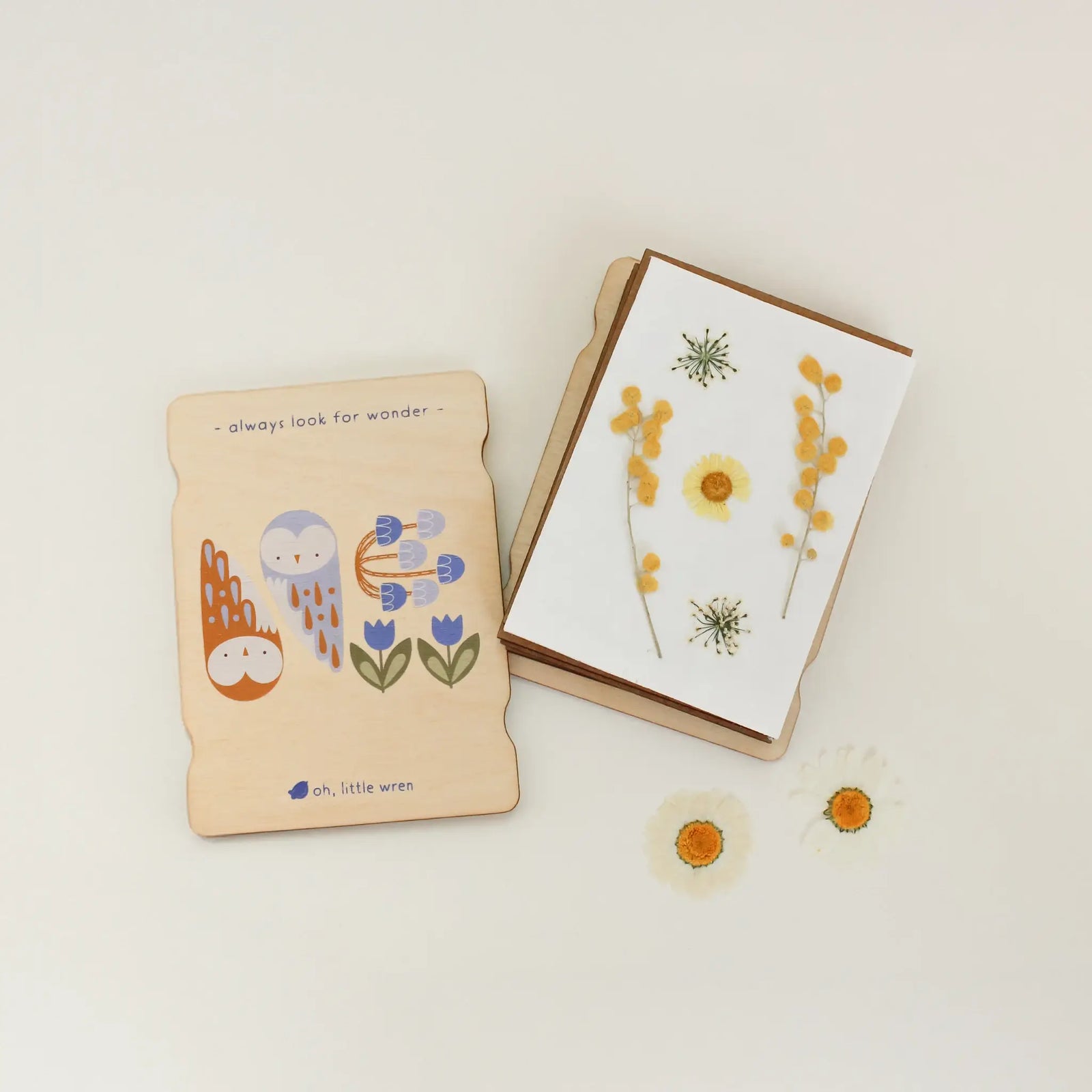 Wooden flower press with illustrations and text 'always look for wonder' on a light background with flowers.