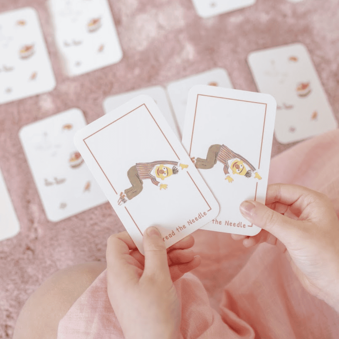 Two hands holding a card with an illustration on a pink surface with more cards.