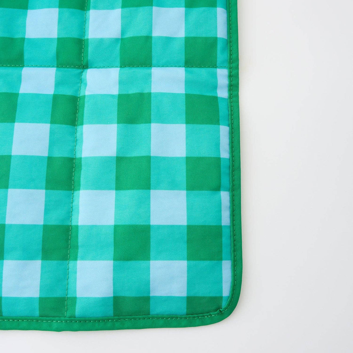 A close-up of a green and light blue gingham quilted mat with a solid green stitched border, shown on a plain white background.