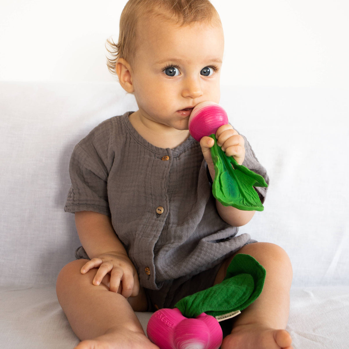 Baby sitting on a white surface holding a pink toy