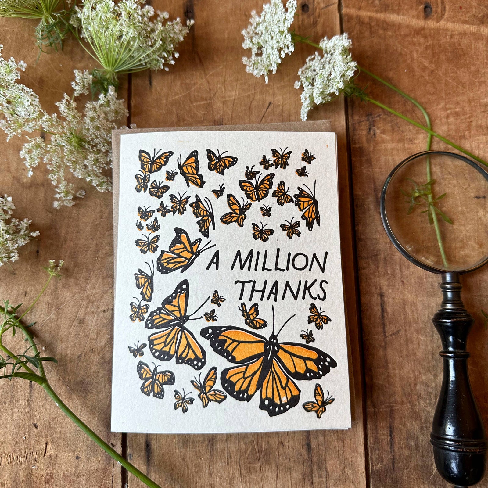 Card with butterfly design and 'A Million Thanks' text on a wooden surface with flowers and a magnifying glass.