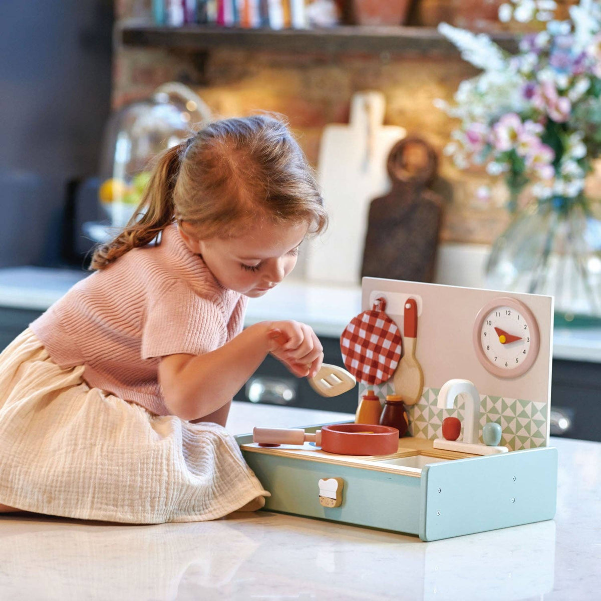 Child playing with a wooden toy kitchen set in a cozy room.