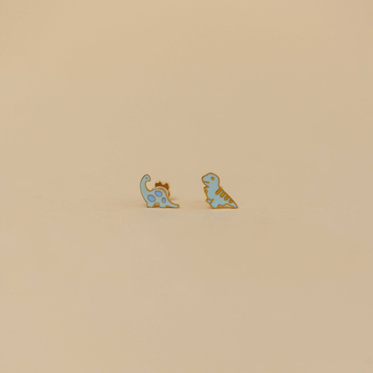 Two dinosaur-shaped earrings on a beige background