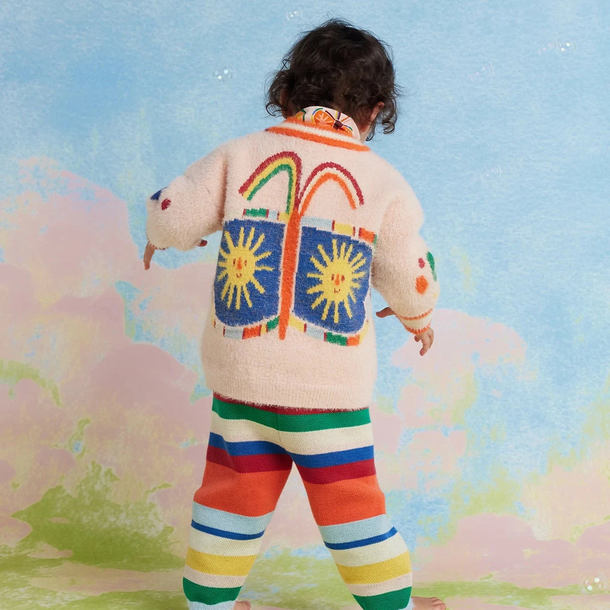 Child wearing a colorful outfit with abstract designs against a pastel background