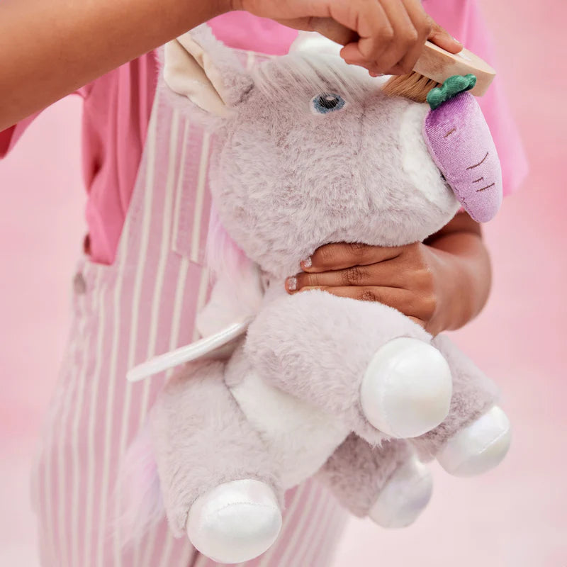 Child holding a plush unicorn toy with a brush against a pink background