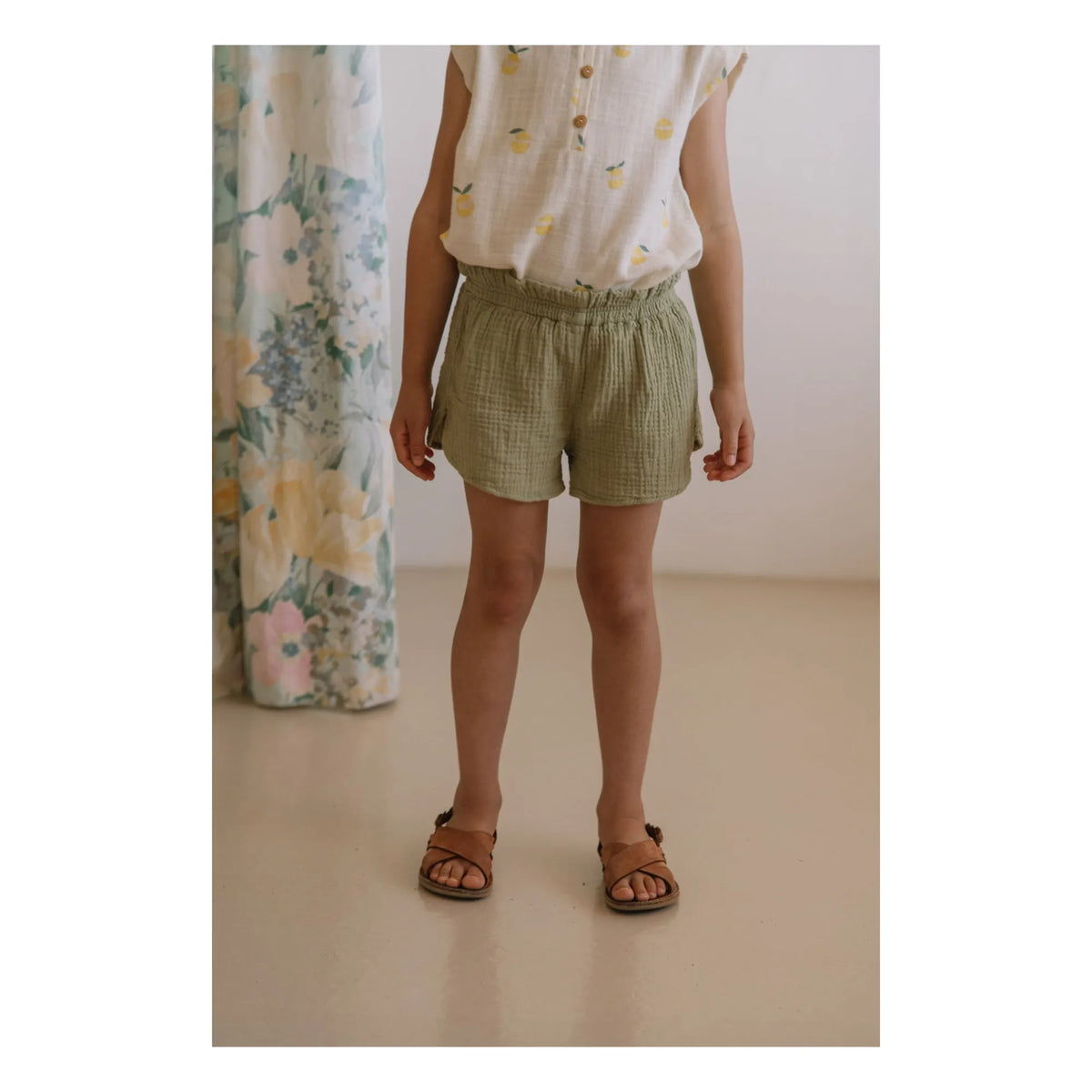 Person wearing green shorts and a white shirt with yellow patterns, standing against a neutral background.