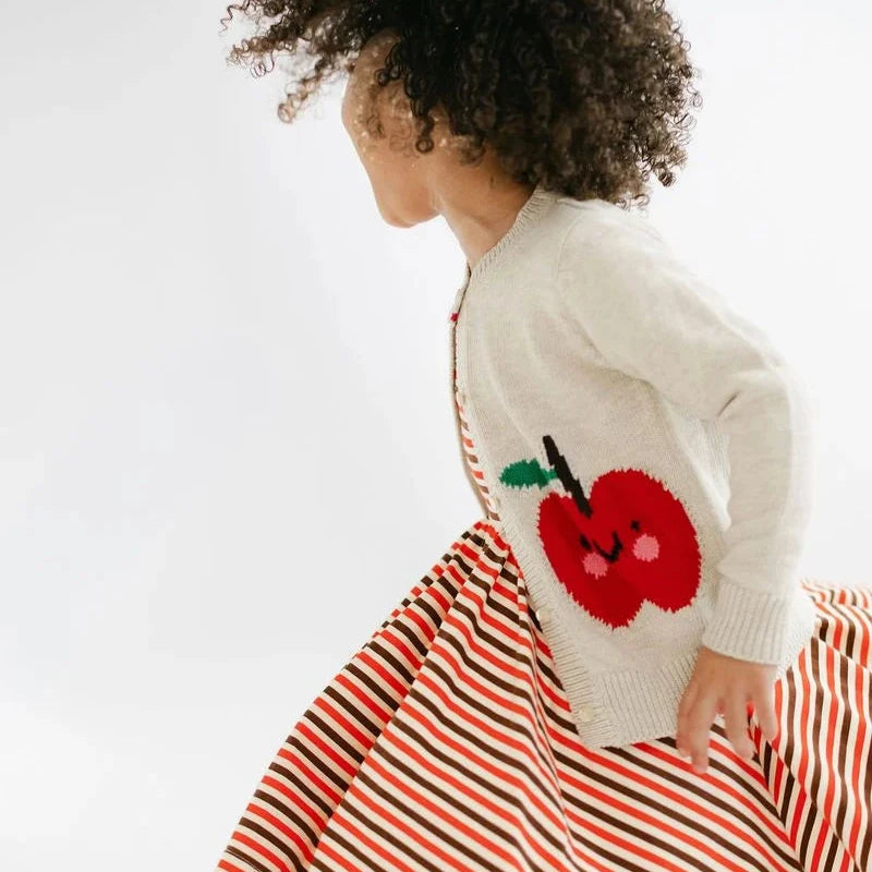 Child wearing a white sweater with a red apple design and a red and orange striped skirt on a white background