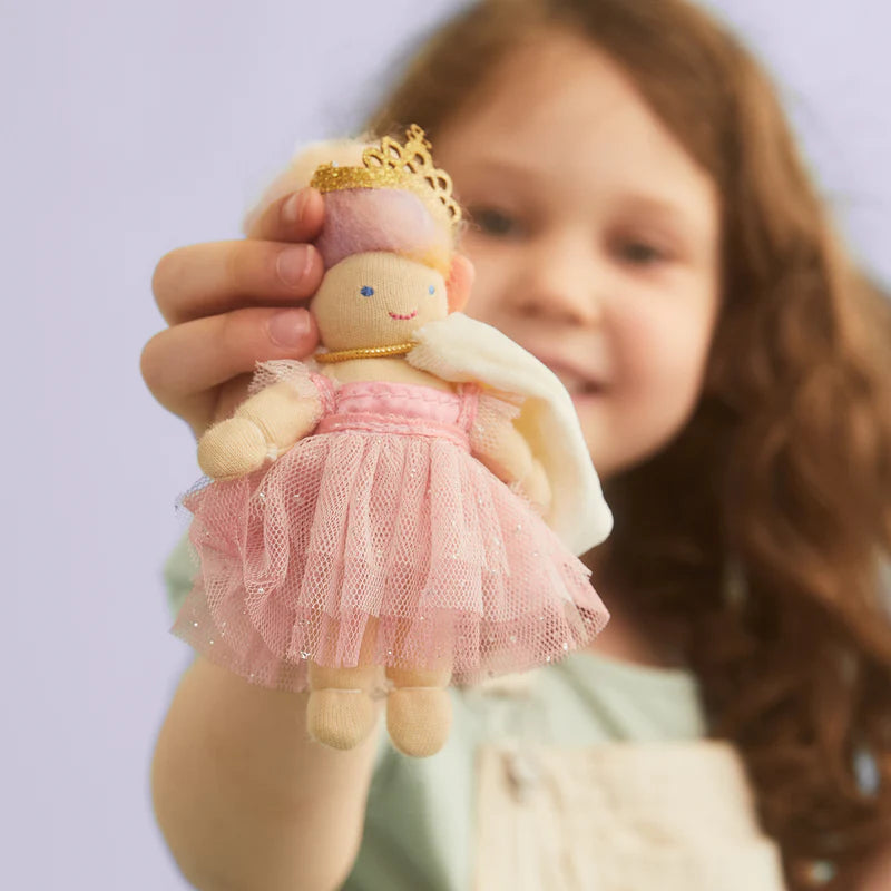 Child holding a small fairy doll with a pink dress and gold crown against a light purple background
