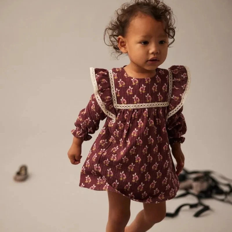Child wearing a patterned dress with lace trim on a plain background