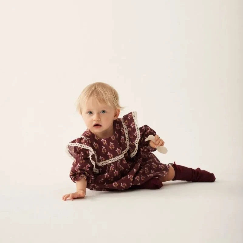 Baby in a patterned dress sitting on a white background