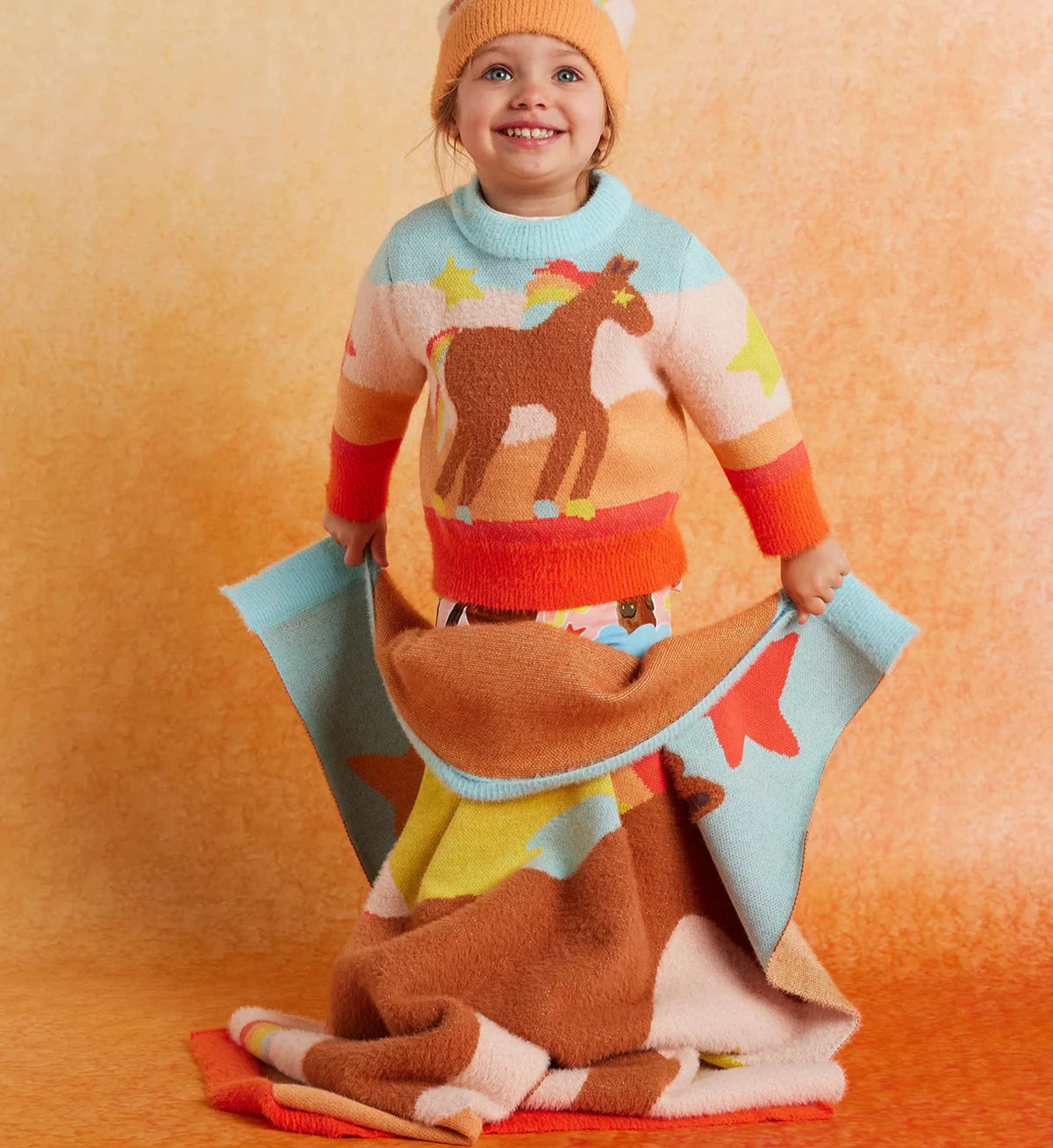 Child wearing horse print sweater holding  blanket with horse print