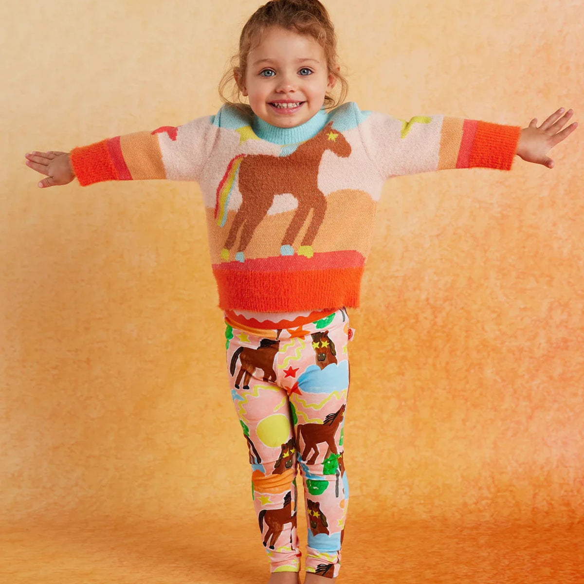 Child wearing horse print sweater with matching pants in bright colors
