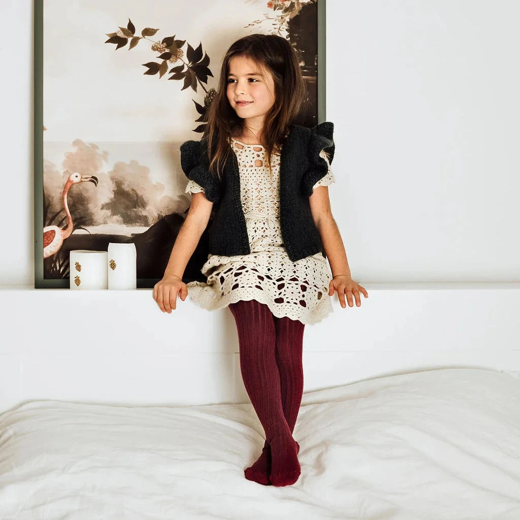 Young girl in a black and white outfit standing on a bed with a framed picture in the background