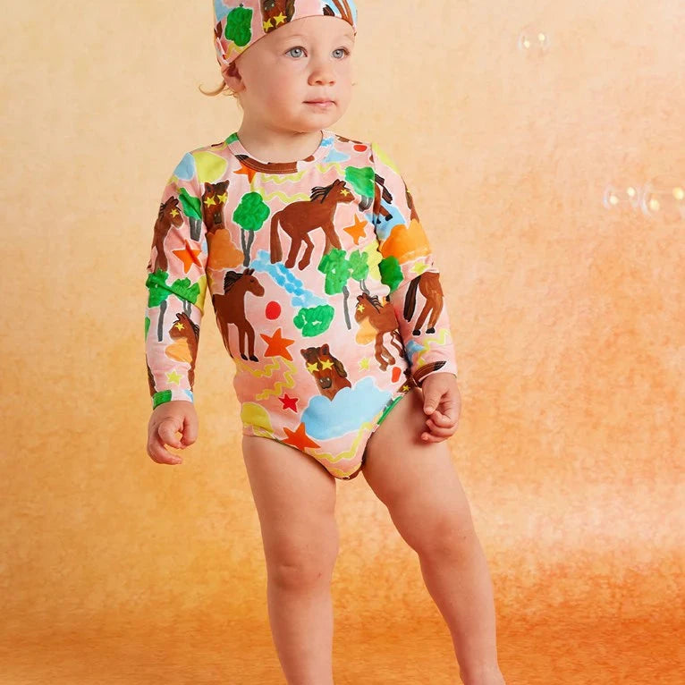 Child wearing a colorful animal-themed bodysuit on an orange background