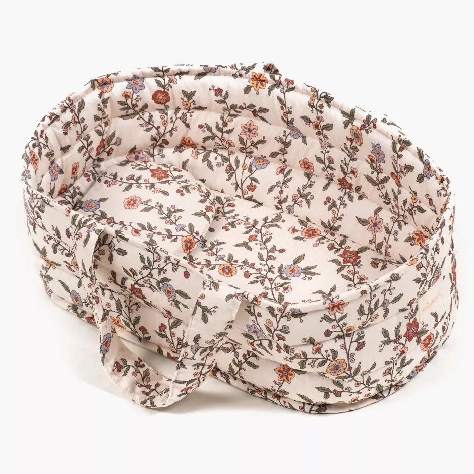 Baby doll in a floral outfit being held by a child laying in a matching floral basket