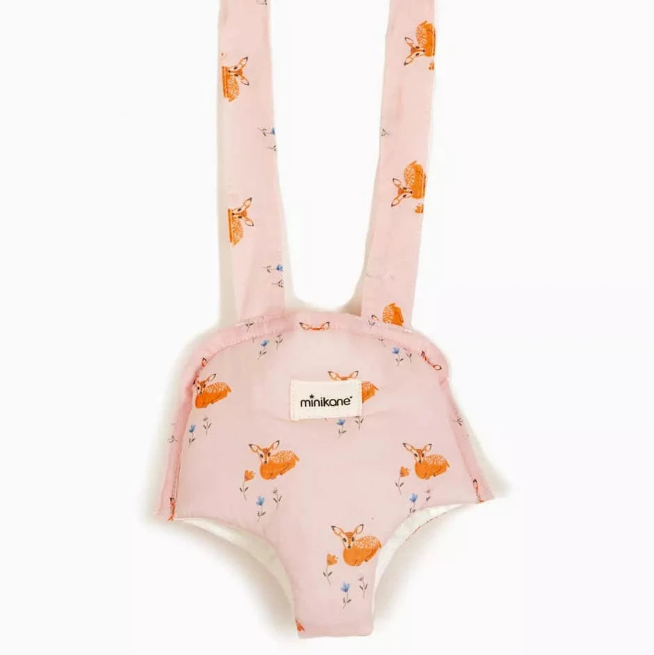 A pink baby doll carrier bag with shoulder straps, featuring an orange and pink deer  print pattern and a white minikane label
