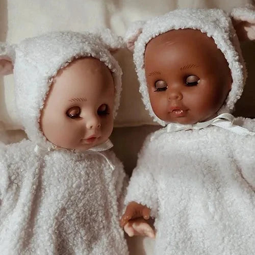 Two dolls in white fuzzy outfits and hats on a soft surface