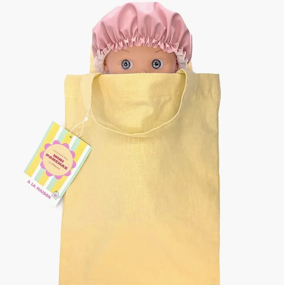 A baby doll with blue eyes wearing a pink satin shower cap and a fuzzy pink and yellow striped bathrobe, standing against a plain white background.