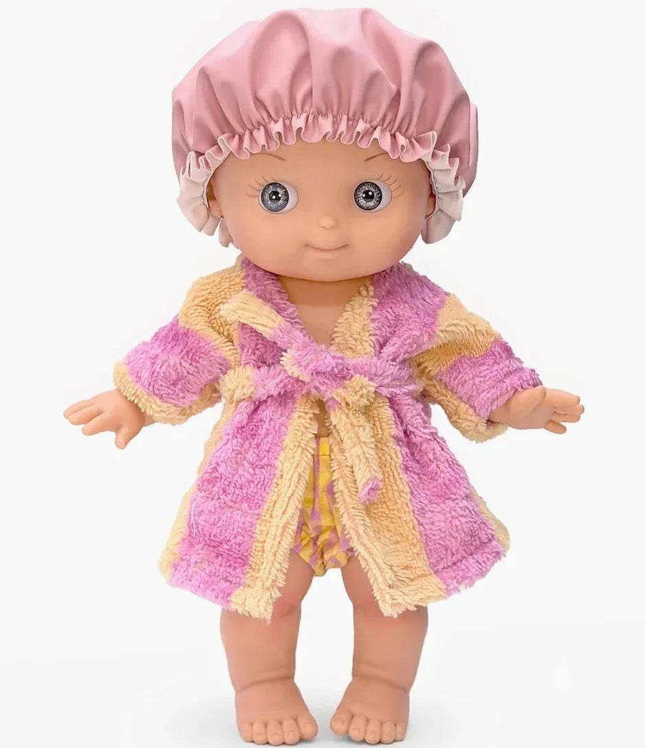 A baby doll with blue eyes wearing a pink satin shower cap and a fuzzy pink and yellow striped bathrobe, standing against a plain white background.