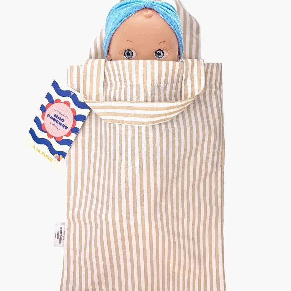 A baby doll in a cream and beige vertically striped fabric carrier pouch, with a blue head wrap and a visible brand tag on the left.