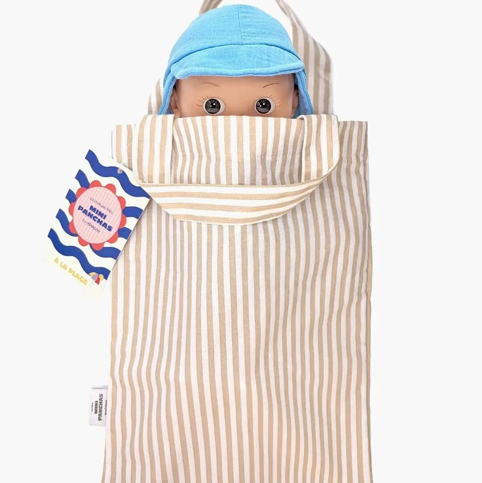 A doll with a blue hat peeking out from a cream and beige vertically striped fabric bag or pouch, shown against a plain light gray background. A blue-and-white paper tag is attached to the left side.