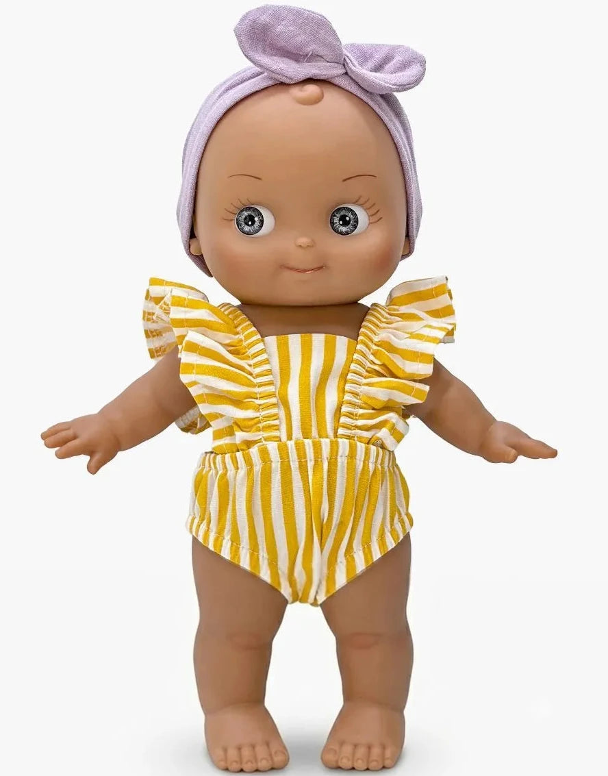 A baby doll with a purple bow headband and a yellow and white striped romper, standing against a light gray background.