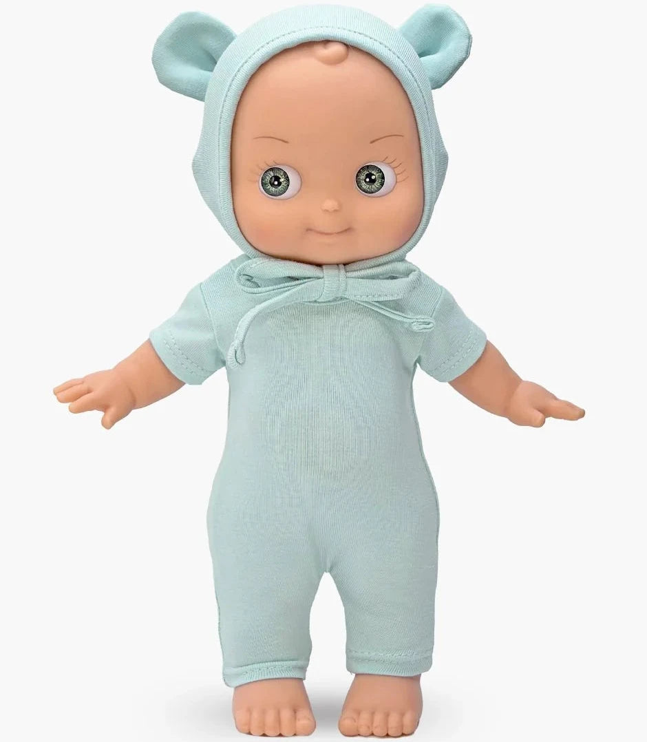 A baby doll wearing a light blue knit hooded romper with bear ears and a small bow, posed against a plain light gray background.