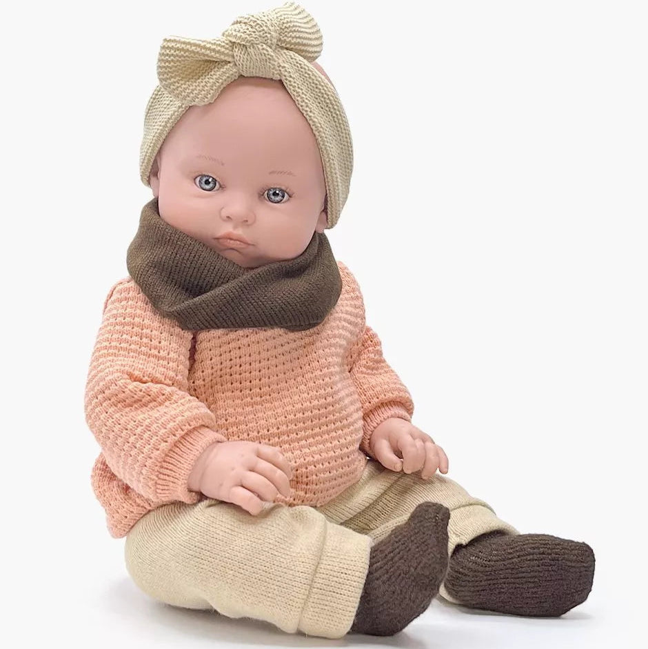 Baby doll wearing a pink knitted outfit with a brown scarf and beige hat on a white background