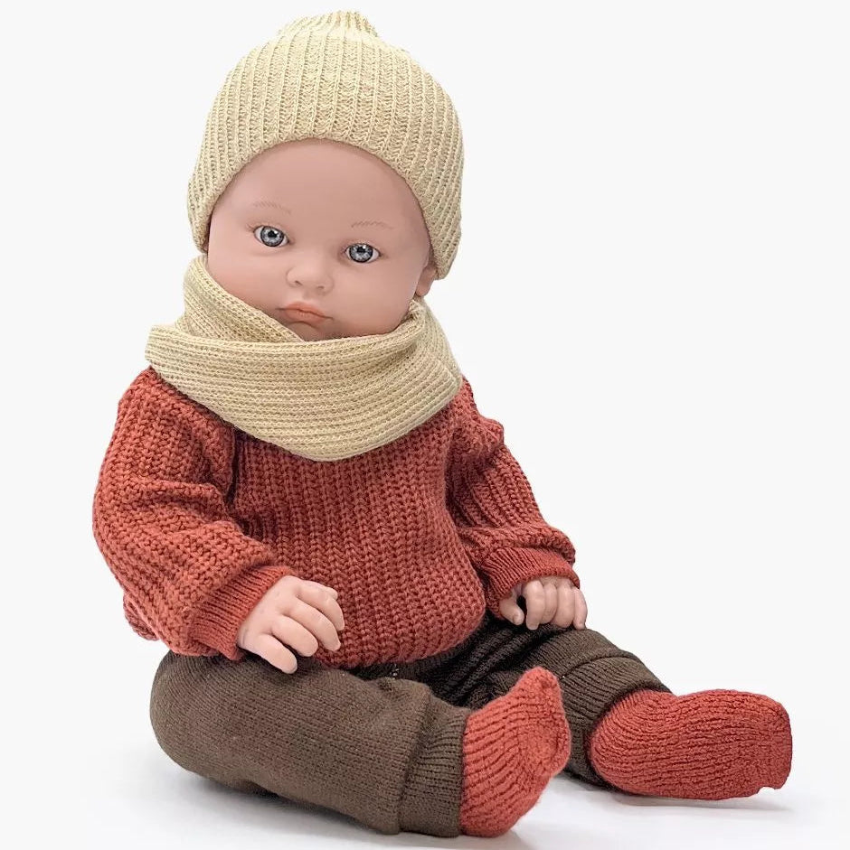 Baby doll wearing a red sweater, brown pants, and beige hat and scarf on a white background