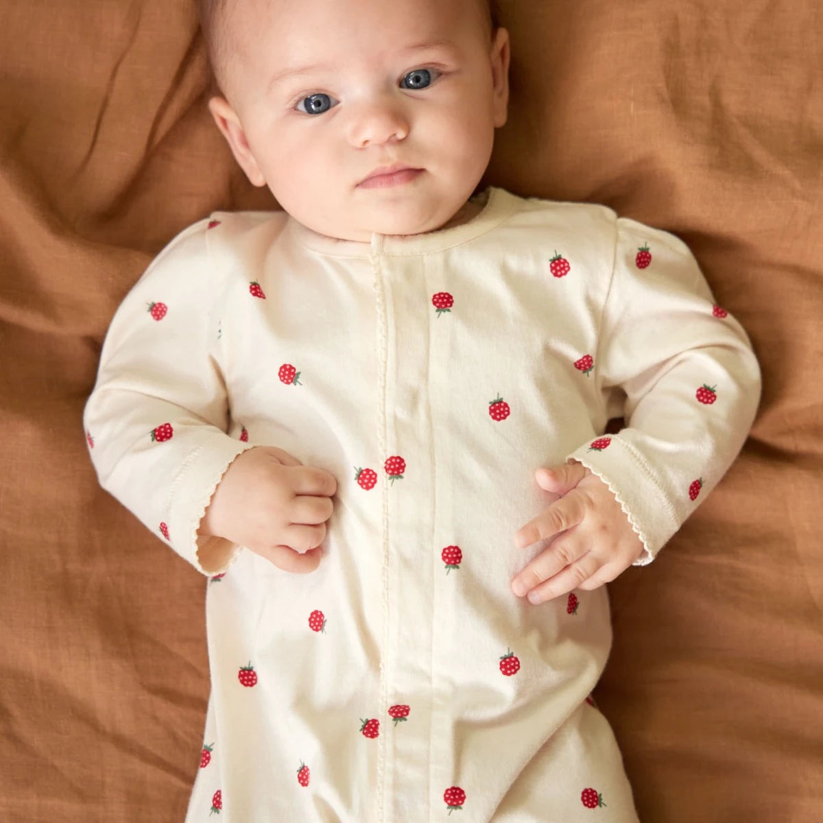 Baby wearing a cream-colored outfit with red berries on a brown fabric background