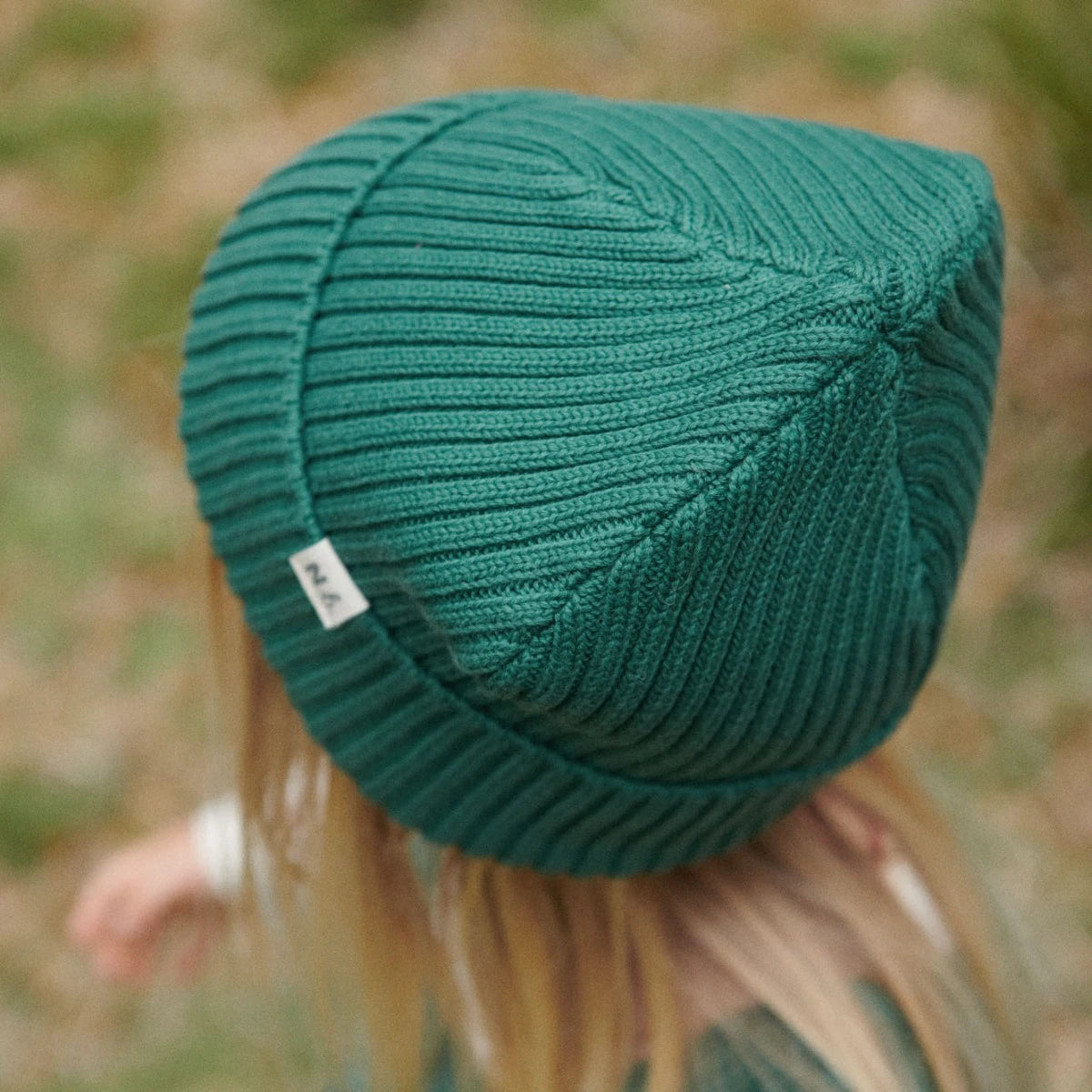 Green knitted beanie worn by a child with a blurred natural background
