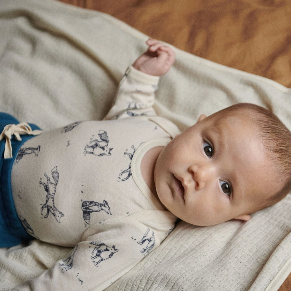 Baby lying on a blanket wearing a fox patterned outfit.