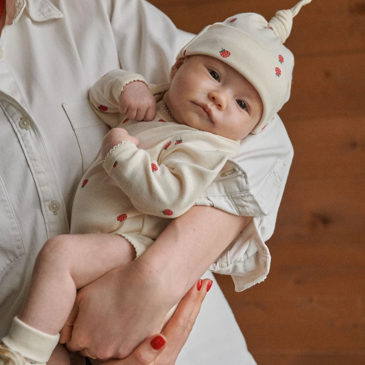 Baby in a matching raspberry print outfit with a person holding them, set against a wooden background.