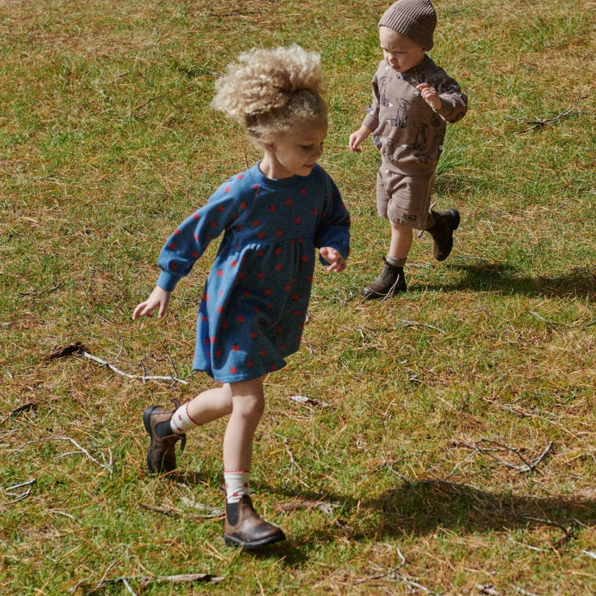 Child wearing a blue dress with red berries and a red beanie against a green background