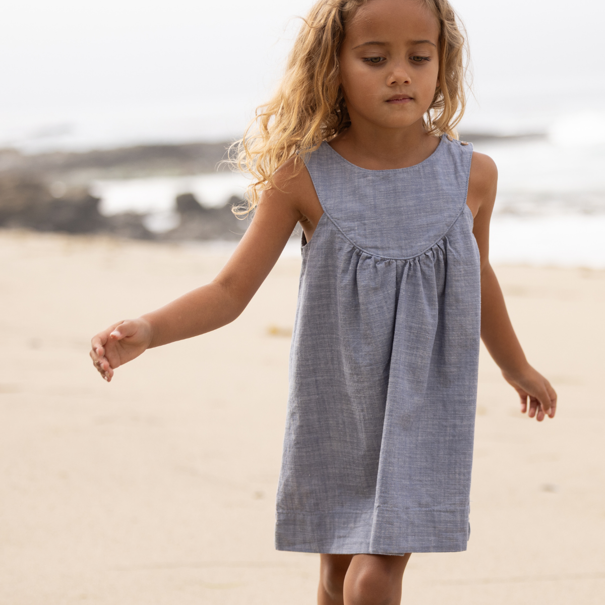 Young girl in a blue dress standing on a sandy beach.