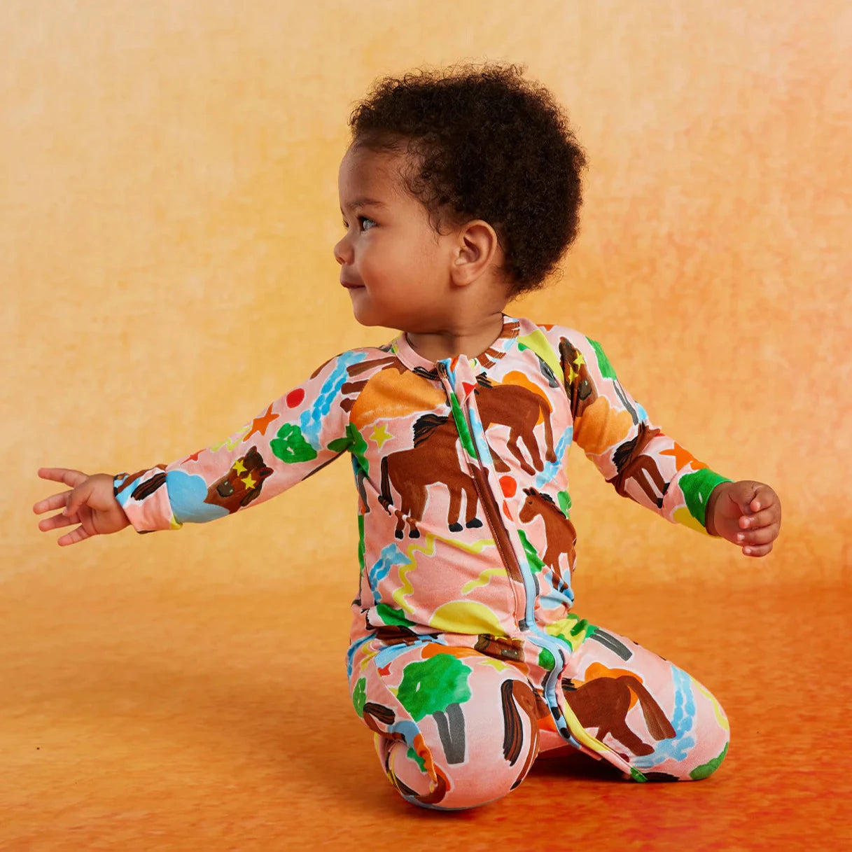 Child wearing a colorful animal-patterned onesie on an orange background