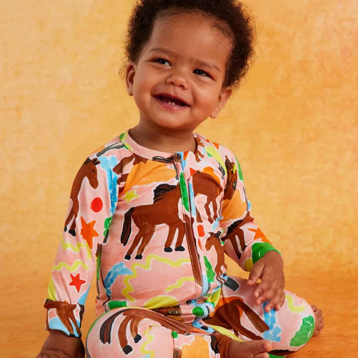 Child wearing a colorful animal-patterned onesie on an orange background