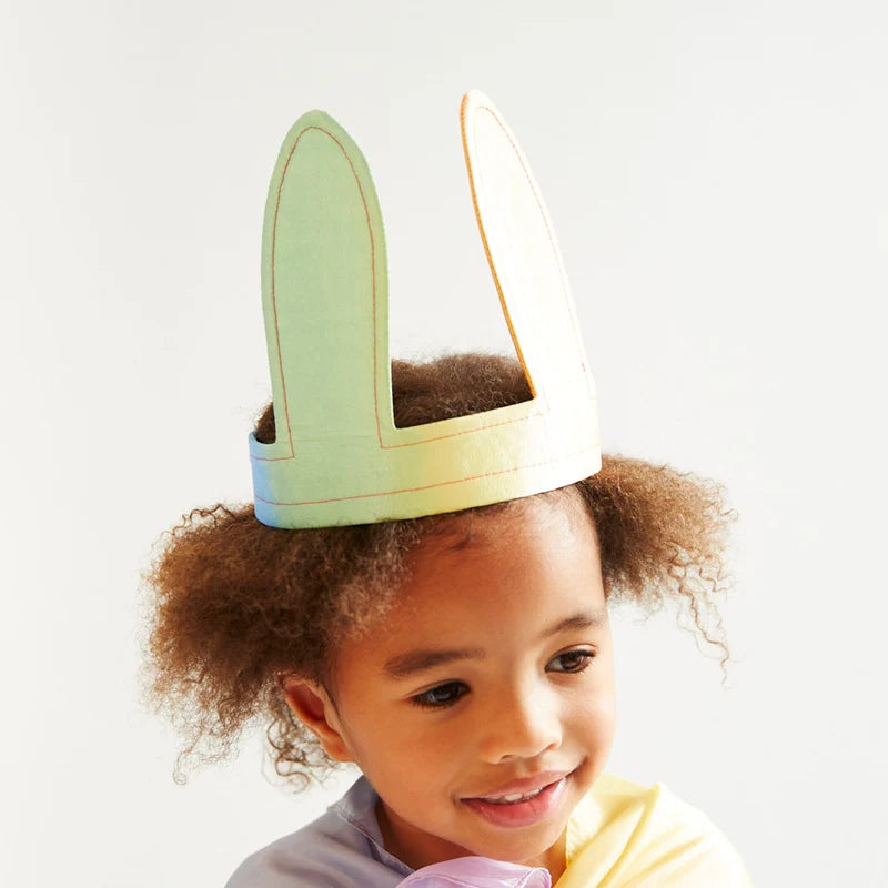A young child with curly brown hair wearing silk bunny-ear headband against a plain white background.