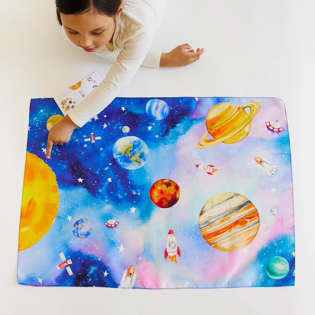 Child playing with space-themed mat featuring planets and rockets on a white background
