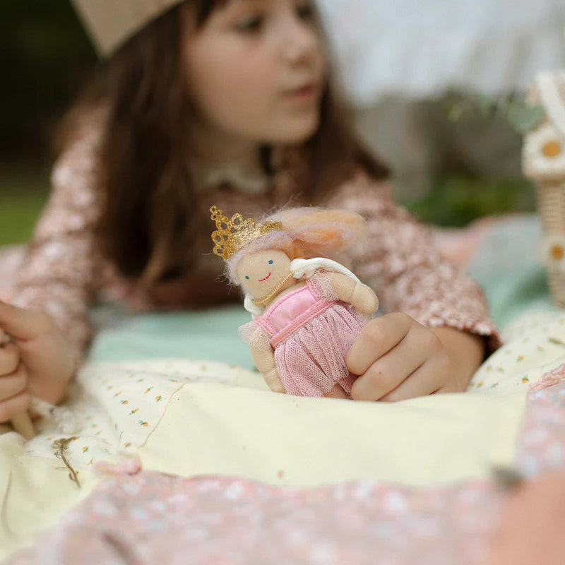 Child holding a small fairy doll with a pink dress and gold crown against a light purple background