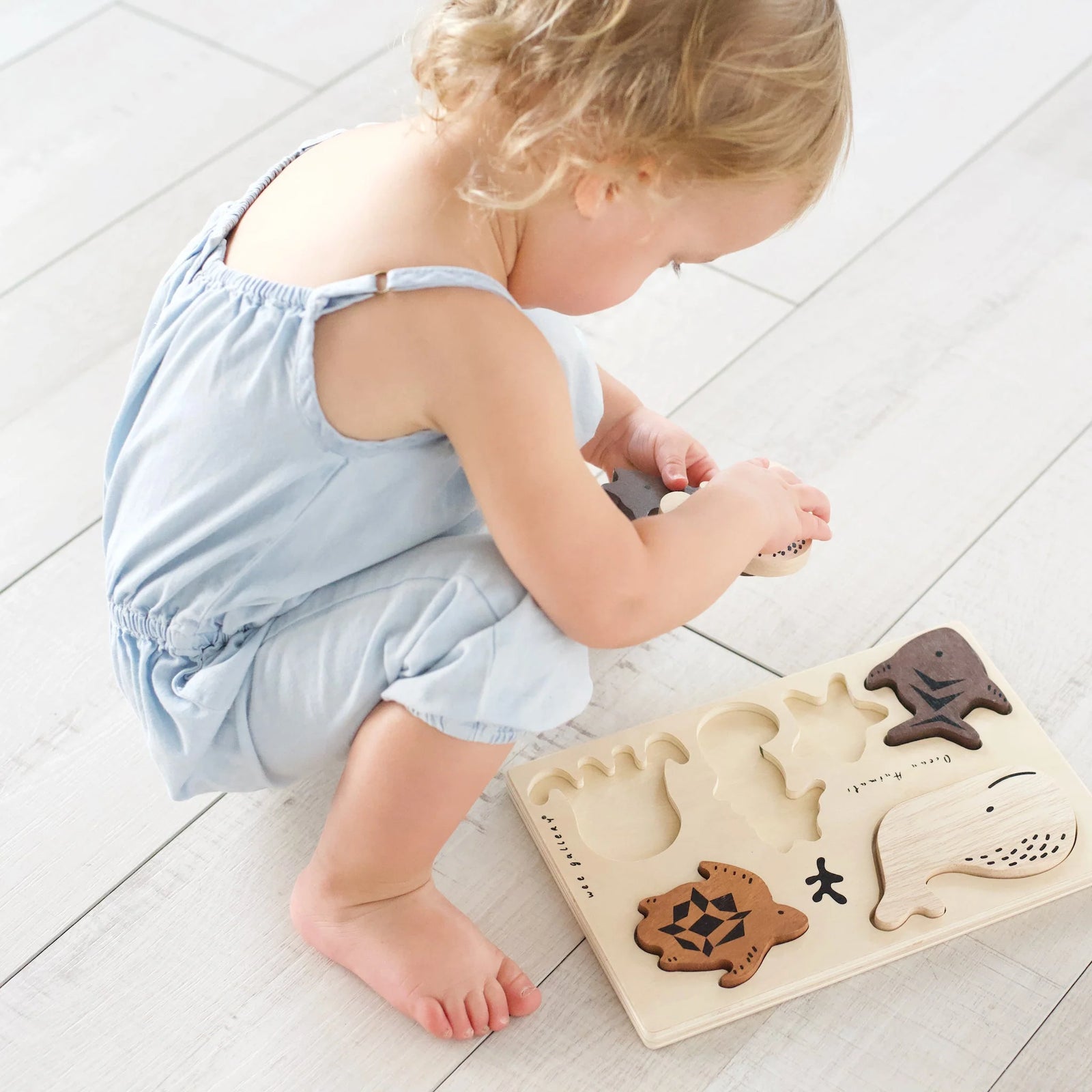 A wooden puzzle tray with various ocean-themed shapes including a whale, seahorse, crab, and star, along with a turtle and fish
