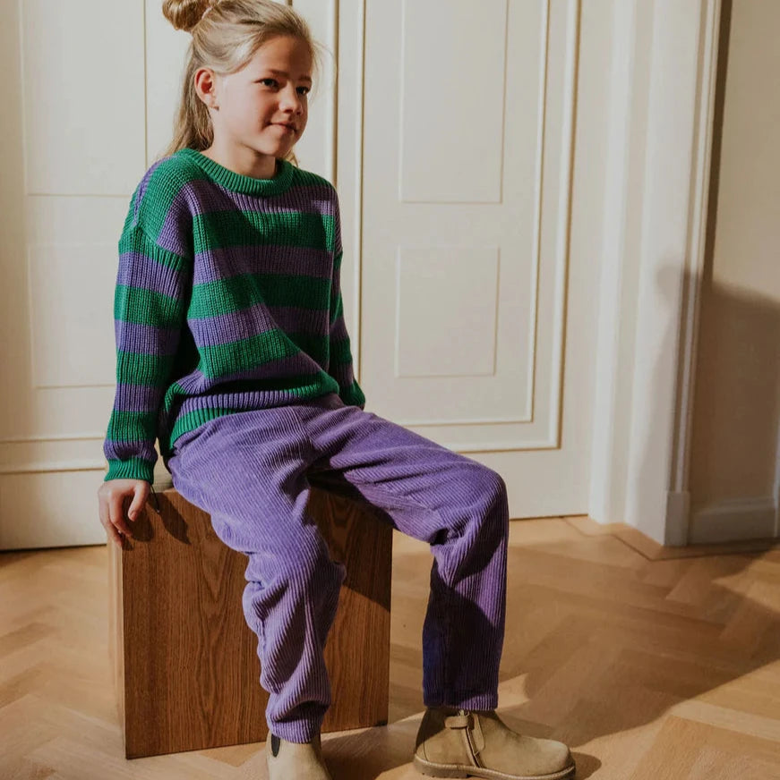 Woman wearing a patterned cardigan and pink pants sitting on a green couch.