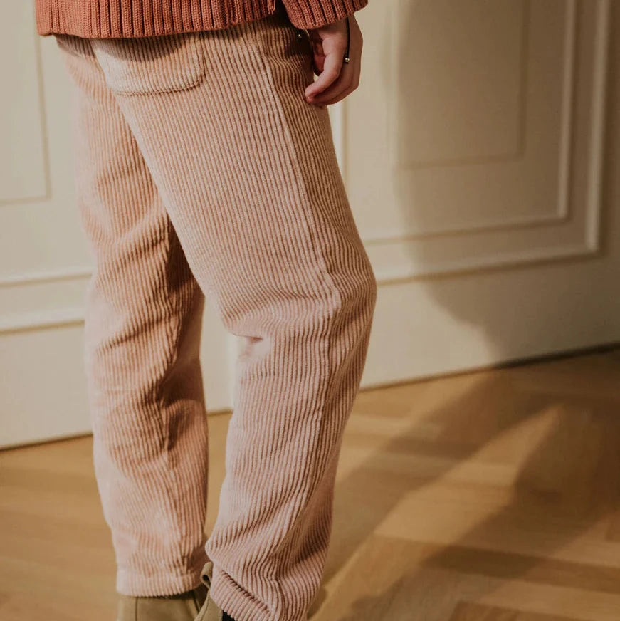 Person wearing a rust-colored sweater, vintage pink corduroy pants, and brown boots on a wooden floor.