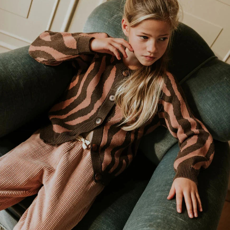 Woman wearing a patterned cardigan and pink pants sitting on a green couch.