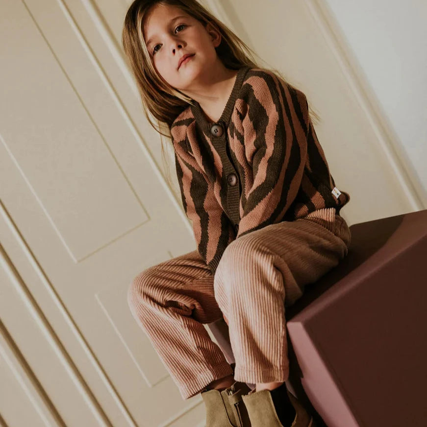Child sitting on a pink stool against a white paneled wall