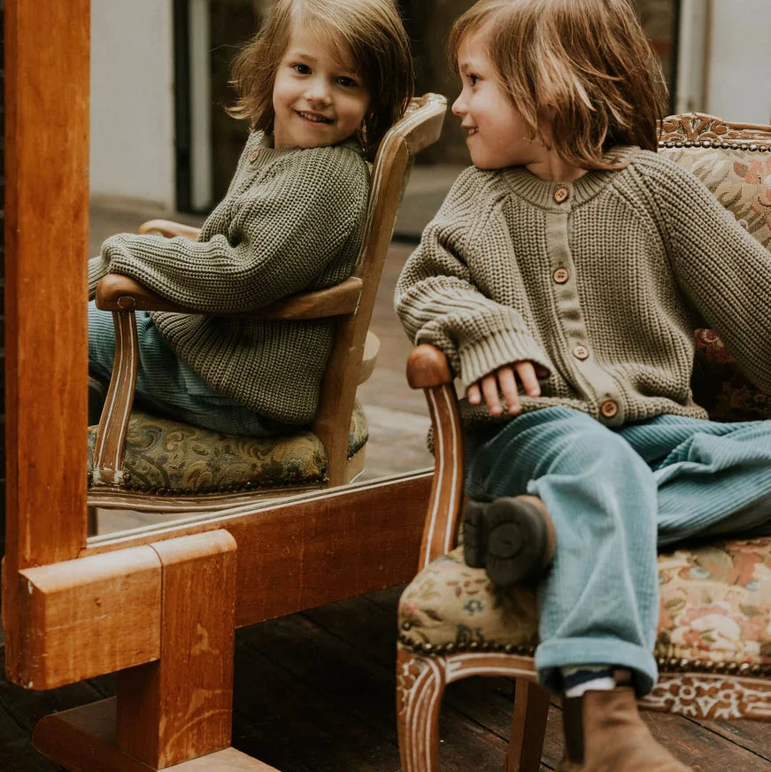 Child sitting on a chair next to a mirror, reflecting their own image.
