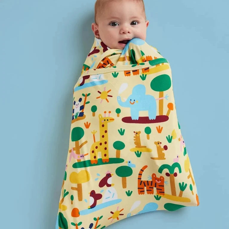 A baby wrapped in a soft safari-themed swaddle blanket, with their face peeking out from the top. The blanket features a light yellow background with colorful animals including a giraffe, elephant, tiger, and zebra, along with trees and suns, set against a solid light blue background.