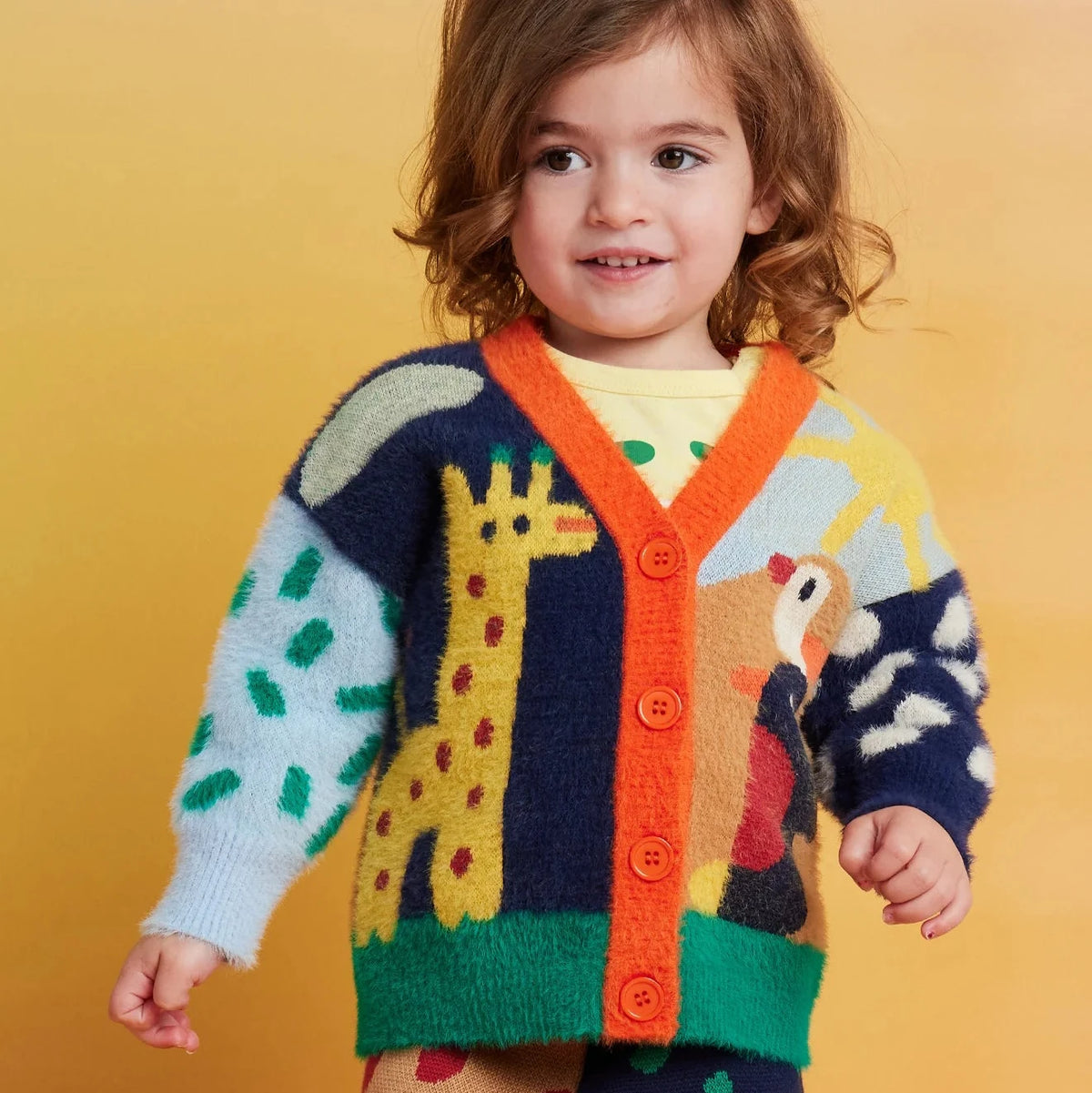 Child wearing a colorful sweater with animal designs on a yellow background